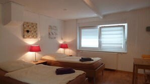 Una habitación con dos camas, una ventana con persianas y dos lámparas fijadas a la pared.