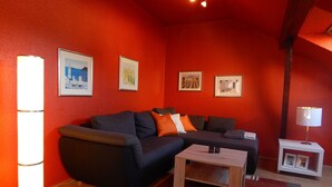 A living room with a dark sofa, a small wooden table, and a red carpet. There are framed pictures on the wall and a lamp on a side table. - Holiday Apartment 'Ferienhaus Rheinblick Wohnung 4' with Shared Terrace, Wi-Fi and Air Conditioning (Koblenz)