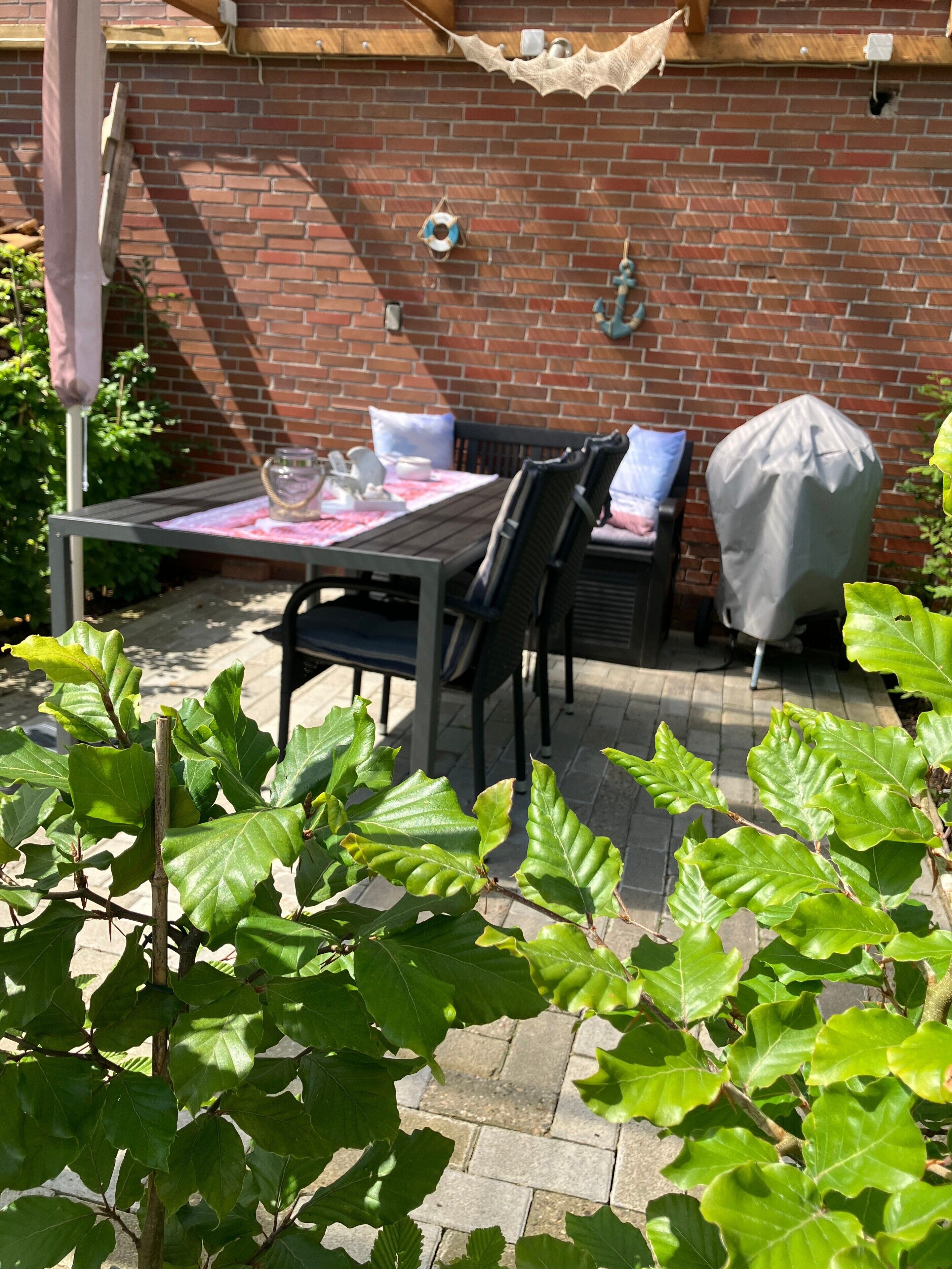 Un mur de briques, une table avec des chaises, un parasol et de la verdure.