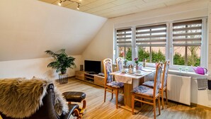 Een eetgedeelte met een tafel, stoelen, een televisie en een raam met jaloezieën.
