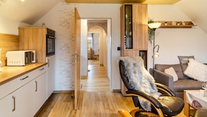 Een ruimtelijk ingerichte leefruimte met kitchenette, eethoek, zithoek met een bont plaid en een trap naar een hoger niveau.