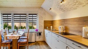 Een moderne keuken met een eettafel, stoelen, een raam met zonwering en een houten spatwand.