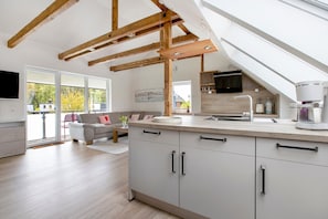 Eine moderne Küche mit einer großen Kochinsel, Holzbalken und Blick ins Freie.