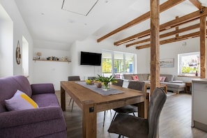 Ein stilvoller Wohnraum mit Esstisch aus Holz, violettem Sofa und einem Wand-Fernseher.