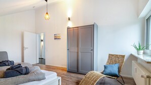 Ein modernes Hotelzimmer mit einem Bett, einem Korbsessel, einem Kleiderschrank und einer Zimmerpflanze.