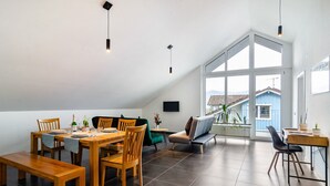 Ein geräumiger Essbereich mit Holztisch und Stühlen, einer Bank und Blick auf ein blaues Haus durch große Fenster.