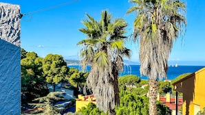 Une vue côtière avec de hauts palmiers, un ciel bleu dégagé et une vue lointaine sur la mer et les montagnes.