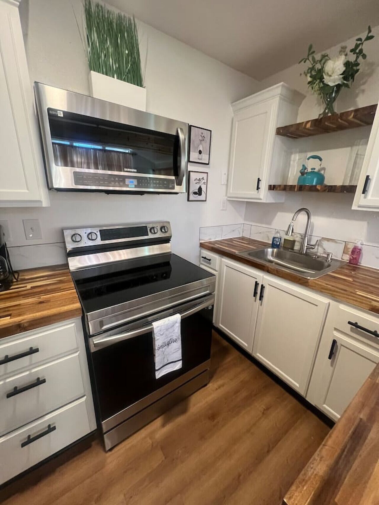 A kitchen with a stainless steel oven, a microwave, and a sink. There are white cabinets and a wooden countertop.
