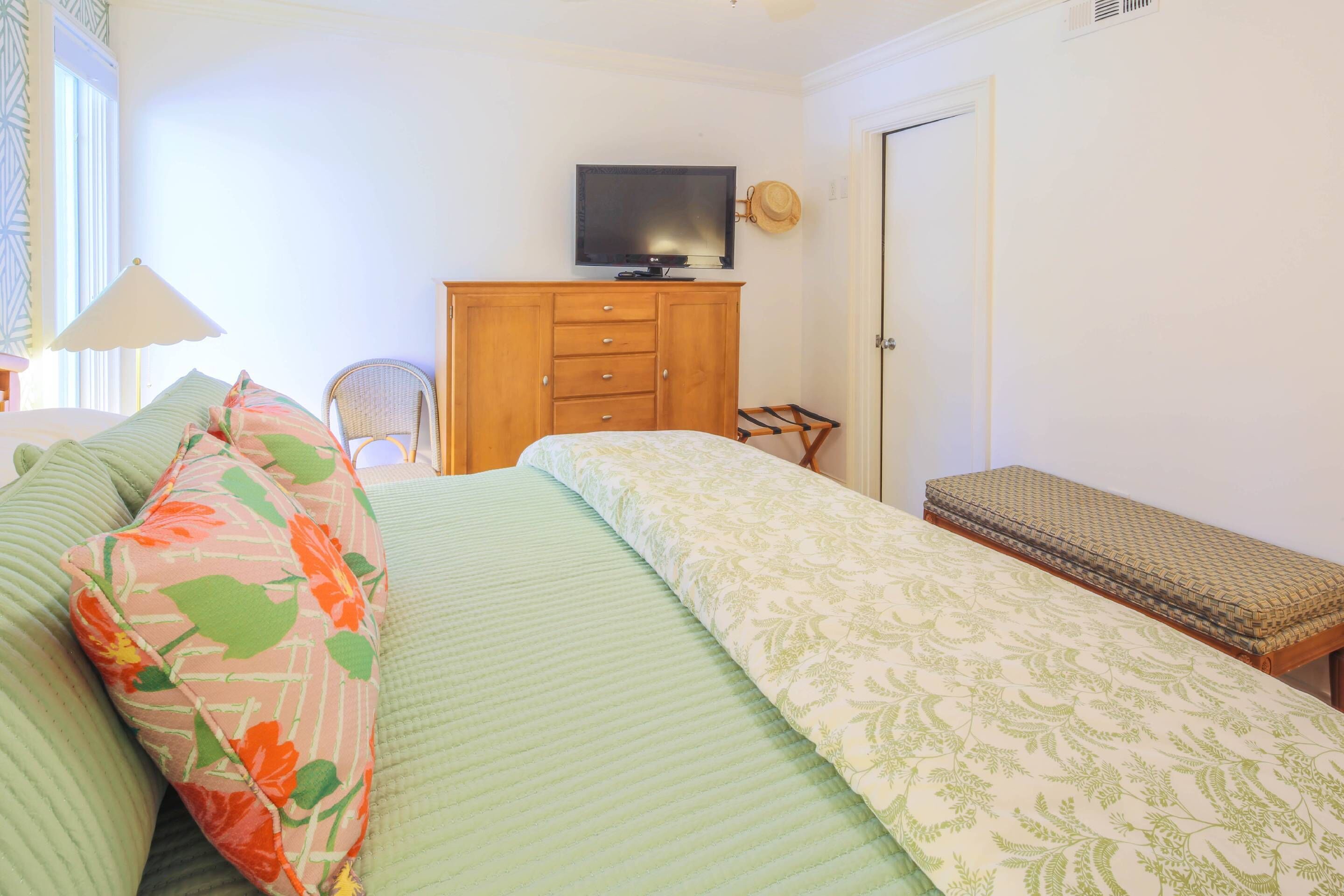 A bedroom with a bed, a wooden dresser, a television, and a bench.