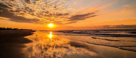 A beach at sunset with a clear sky and calm waves.