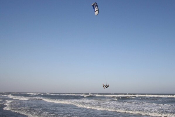 A beach with waves and a kite surfer in the air.