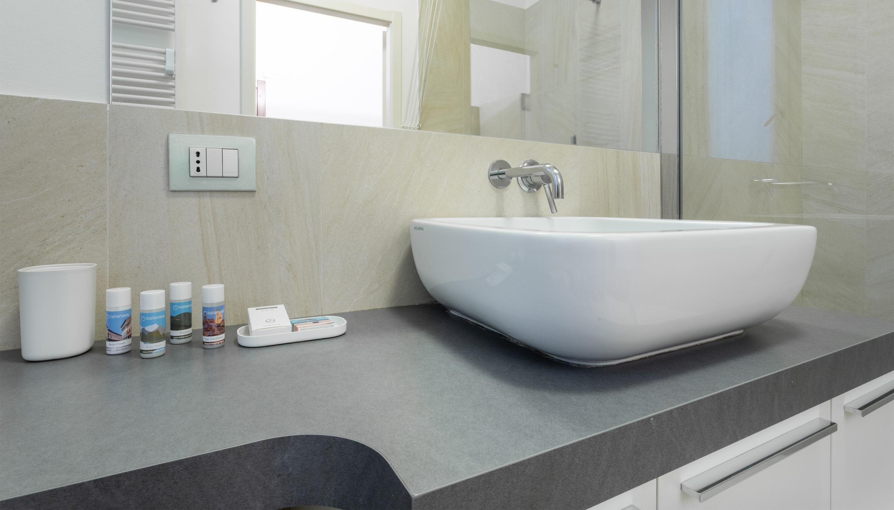 Ein Badezimmer mit einem großen weißen Waschbecken, einem Spiegel und einer Ablage mit Toilettenartikeln.