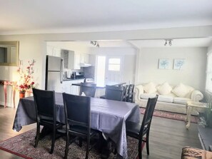 Ein geräumiger Wohnbereich mit Esstisch, Stühlen, einer Couch und einer Küche im Hintergrund.