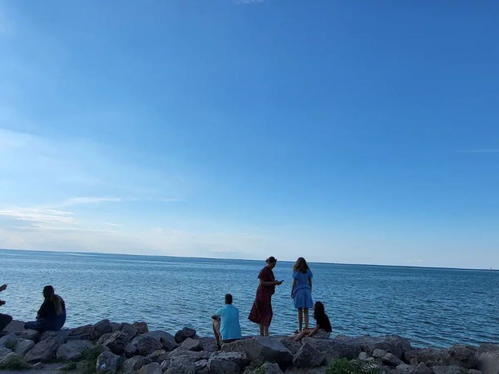 A group of people sitting and standing on a rocky shoreline by the sea.