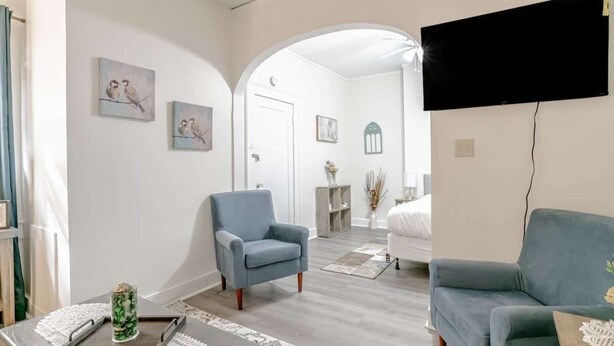 A modern living room with a blue armchair, a grey sofa, and a flat-screen TV mounted on the wall. - Charming Midtown Apt - Hannon Hideaway Unit B (Mobile)
