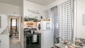 A compact kitchen with a stove, oven, and refrigerator. A dining table with plates and cutlery is set. A 'Welcome' sign is on the wall. - Charming Midtown Apt - Hannon Hideaway Unit B (Mobile)