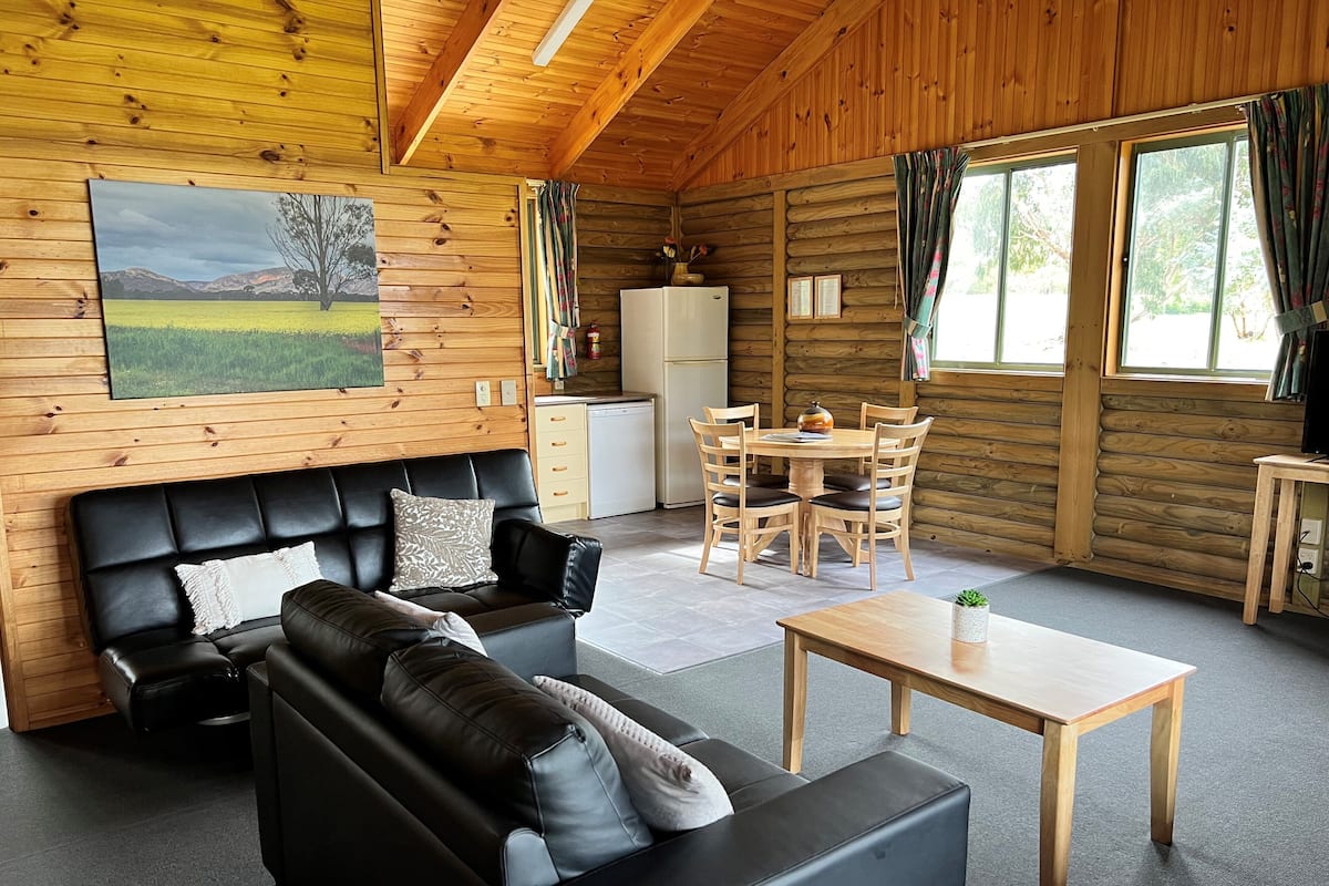 L’intérieur chaleureux d’un chalet avec un canapé en cuir noir, une table à manger en bois et un coin cuisine.