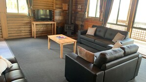 Tunnelmallinen, mökin tyylinen huone, jossa on nahkasohva, puinen sohvapöytä, televisio ja takka.