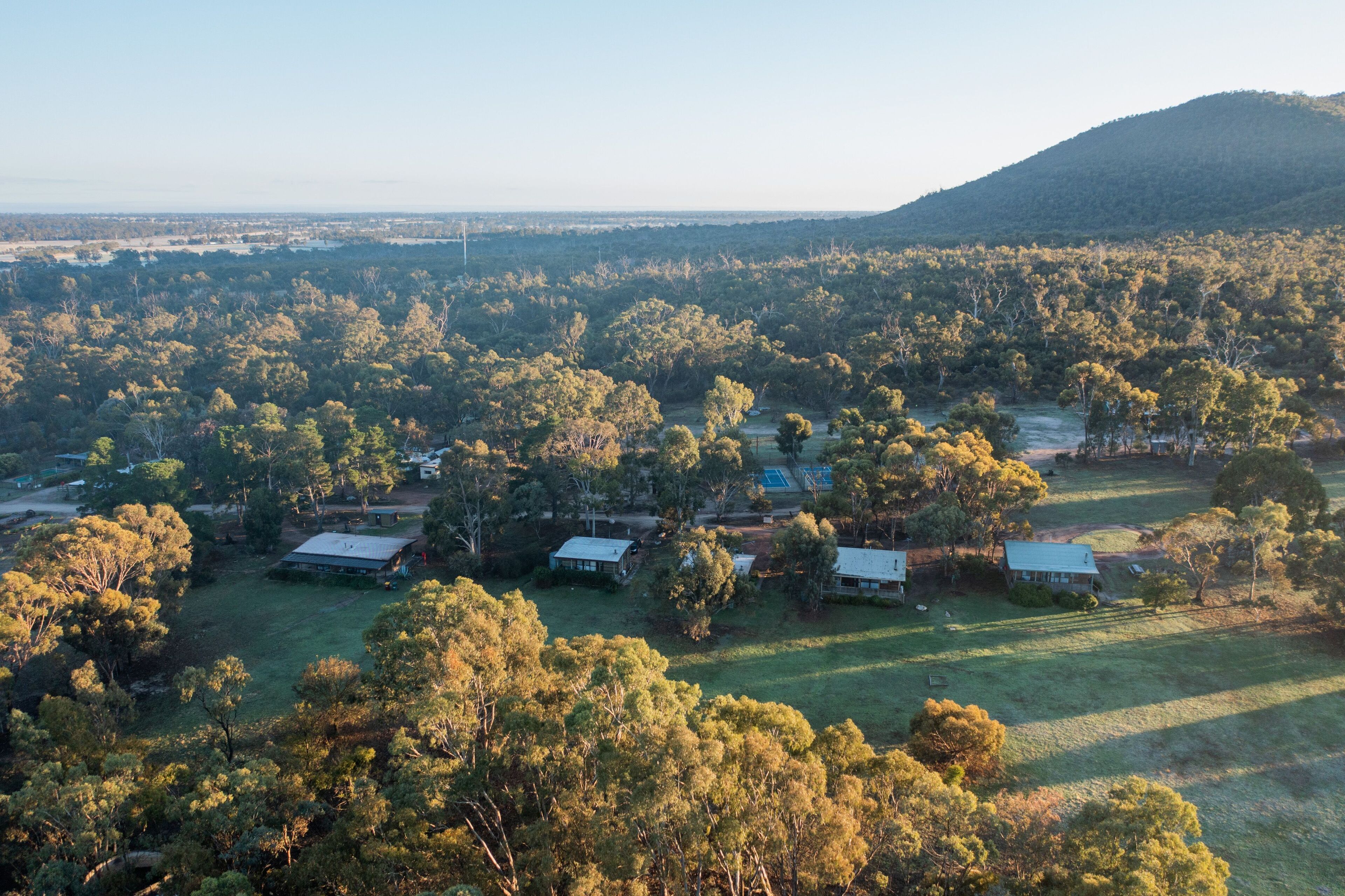 An aerial view of a rural area with scattered houses surrounded by dense forest and open fields.