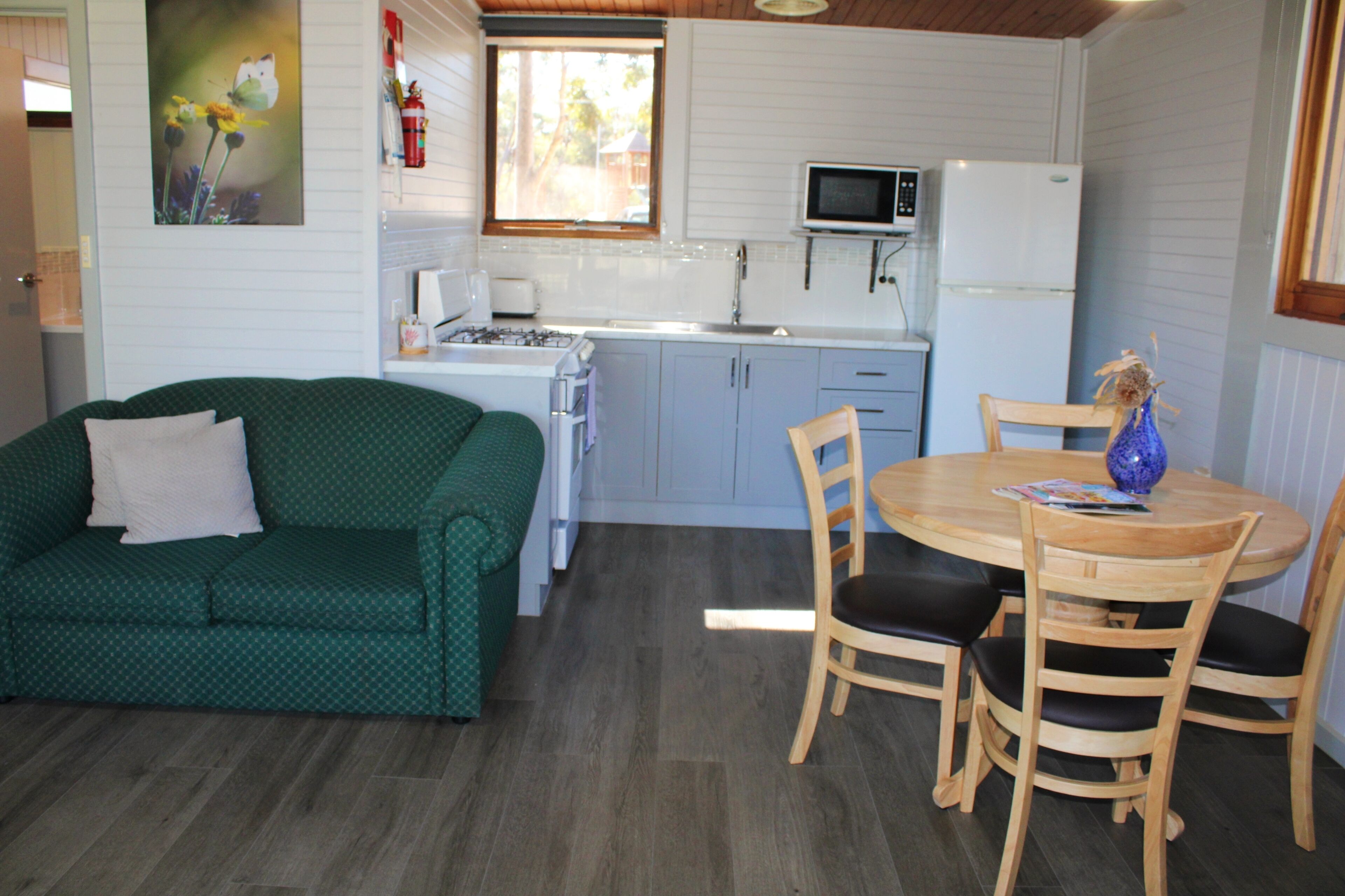 Un espacio habitable compacto con kitchenette, un sofá verde, una mesa de comedor de madera con sillas y un cuadro en la pared.