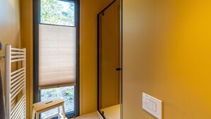 Baño con ducha, perchero y ventana con persianas.