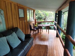 Eine Holzterrasse mit einer schwarzen Ledersofa und einem Tisch mit Stühlen.