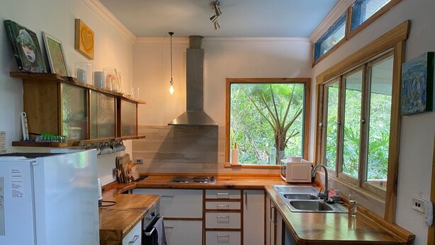 Cocina compacta con horno integrado, microondas, pileta y ventana con vista a vegetación.
