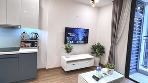 Un salon moderne doté d’un téléviseur à écran plat, d’une table basse avec des télécommandes, d’un canapé et d’un coin cuisine avec des placards et un four à micro-ondes.