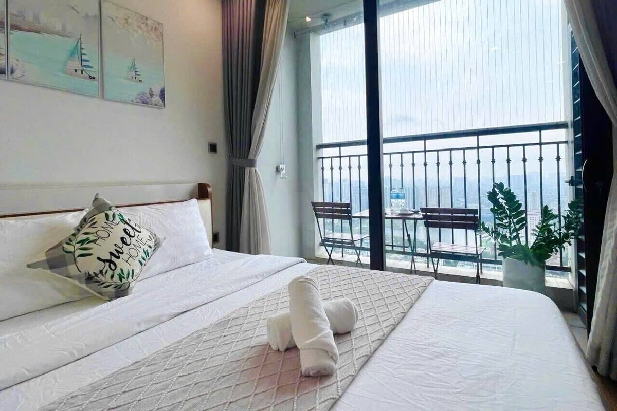 Una habitación de hotel con una cama grande, vistas de la ciudad desde un balcón y una mesa con sillas afuera.