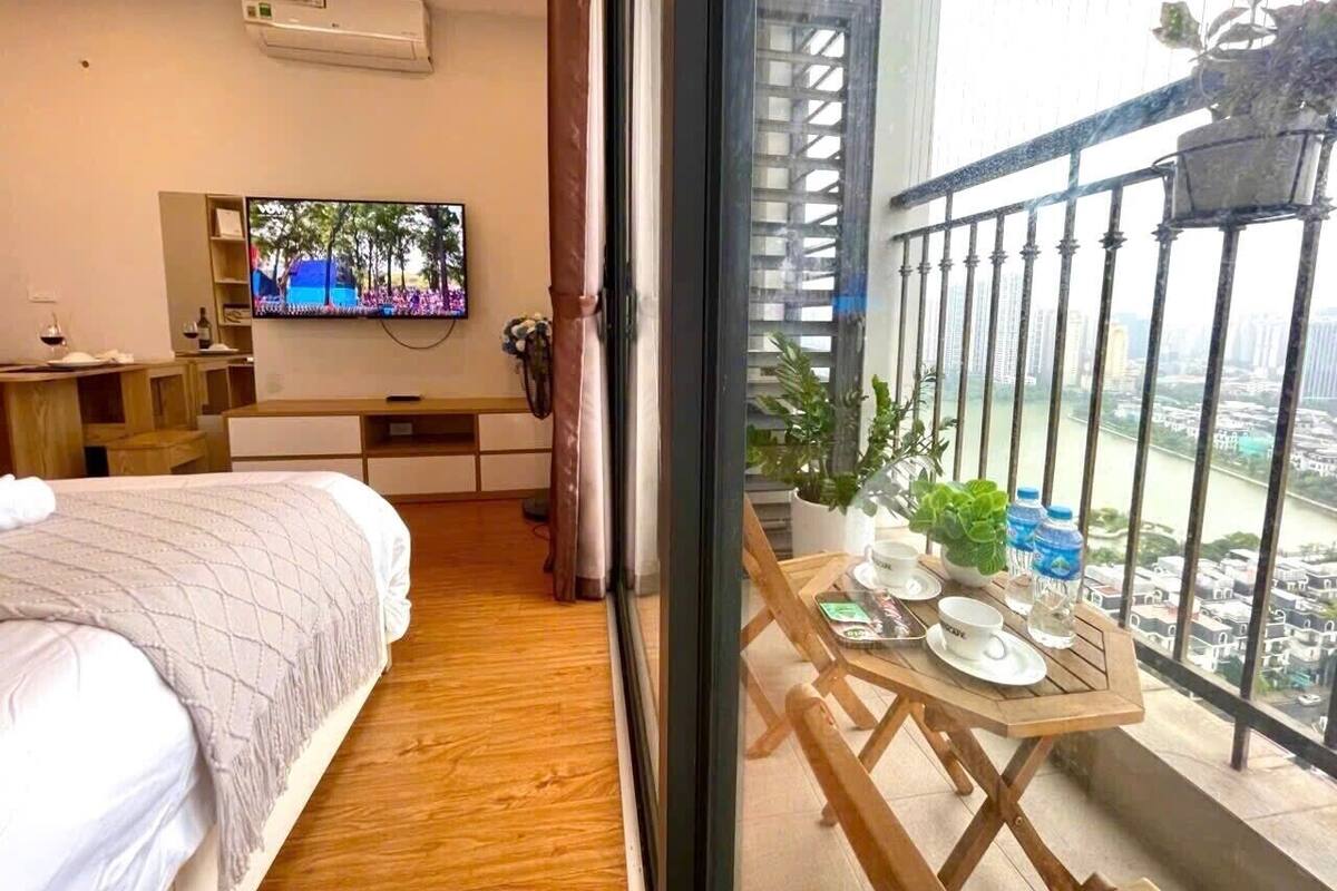 Habitación de hotel con cama, televisión, balcón con mesa y plantas en macetas.