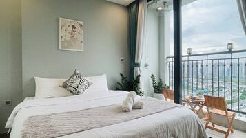Een netjes opgemaakt bed met een kussen en dekbed, een kleine houten stoel en een balkon met uitzicht op de stad.
