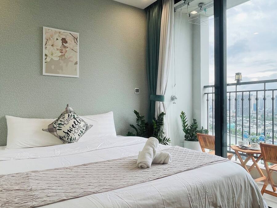Een netjes opgemaakt bed met een kussen en dekbed, een kleine houten stoel en een balkon met uitzicht op de stad.