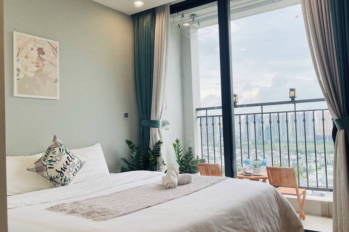 Habitación de hotel con una cama grande, vistas de la ciudad desde un balcón y un cuadro en la pared.