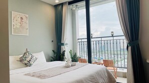 Een hotelkamer met een groot bed, uitzicht op de stad vanaf een balkon en een schilderij aan de muur.