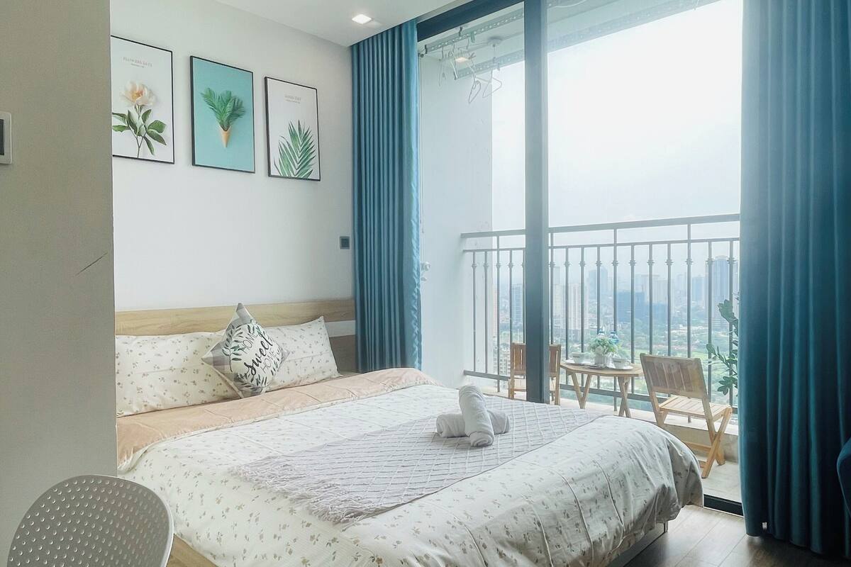 Habitación de hotel con cama, una silla, balcón con vista a la ciudad y tres cuadros en la pared.