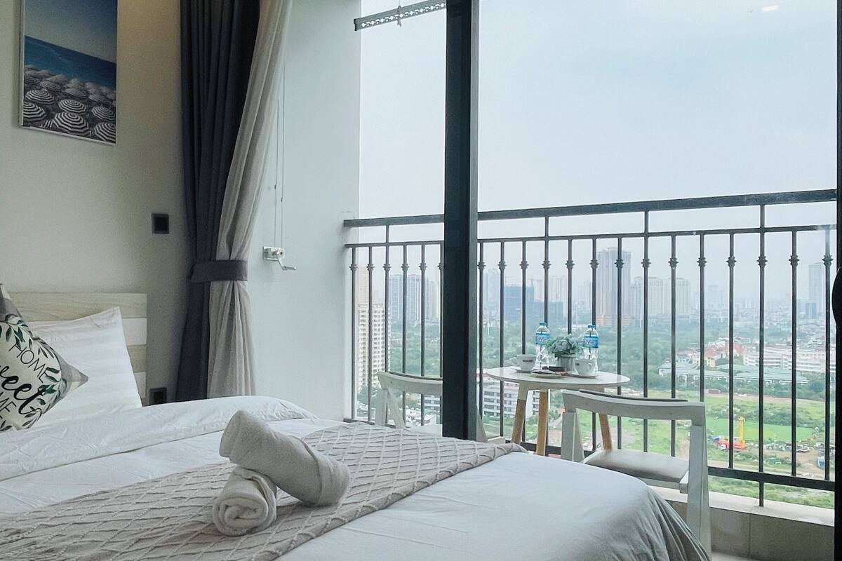 Habitación de hotel con cama, vista de la ciudad desde un balcón y una mesita con botellas de agua.