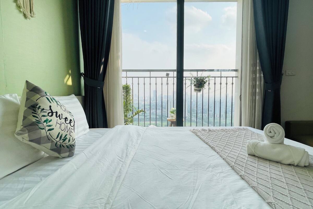 Un cuarto de hotel con una cama, vista de la ciudad a través de un balcón y una ventana con cortinas.