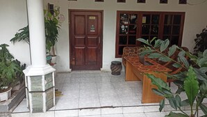 A clean, tiled entrance area with a wooden door, a bench, and potted plants. - OYO Life 91339 Pondok Kost Aulia Syariah (Garut)