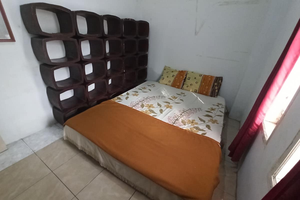 Une chambre à coucher avec un lit, une tête de lit, une fenêtre avec des rideaux et un plancher carrelé.
