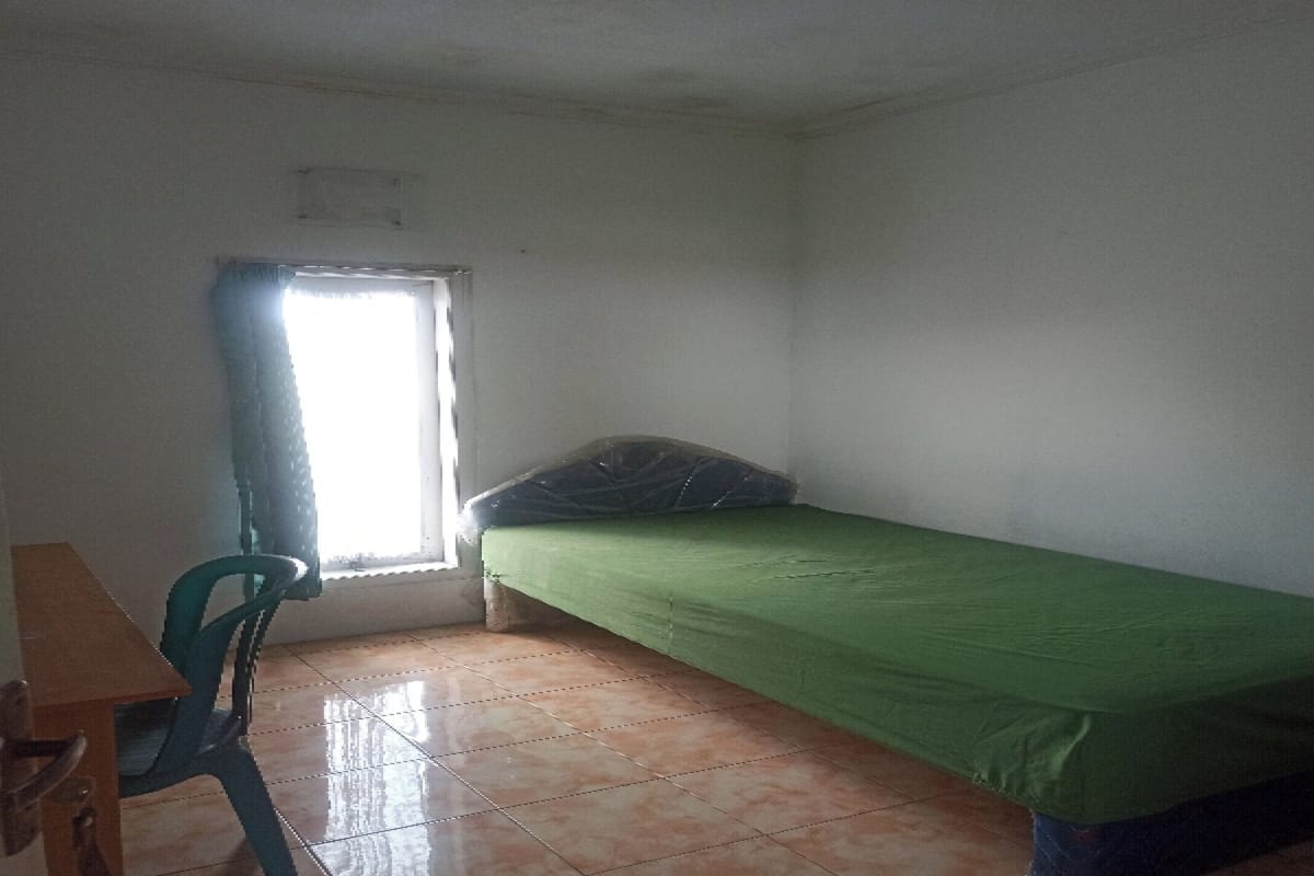 Une petite pièce avec un lit simple, une chaise et une fenêtre.