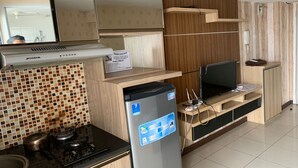 A modern kitchen with a gas stove, a built-in oven, a refrigerator, and a flat-screen TV on a wooden shelf. - OYO Life 93374 Andira Inn (Depok)