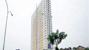 A tall, modern building with a grid-like facade, surrounded by smaller buildings and greenery. - OYO Life 93374 Andira Inn (Depok)