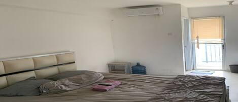 A bedroom with a bed, a water dispenser, a small table, and a window with blinds.