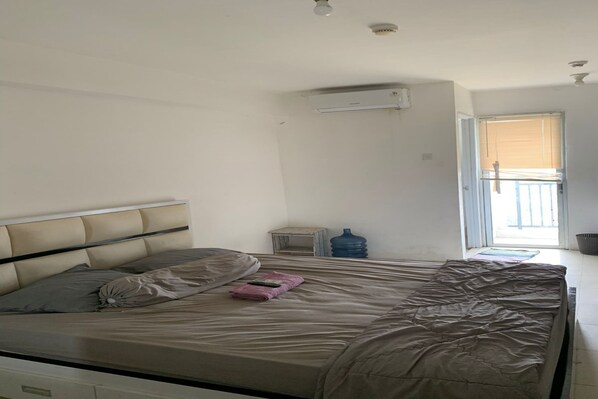 A bedroom with a bed, a water dispenser, a small table, and a window with blinds.