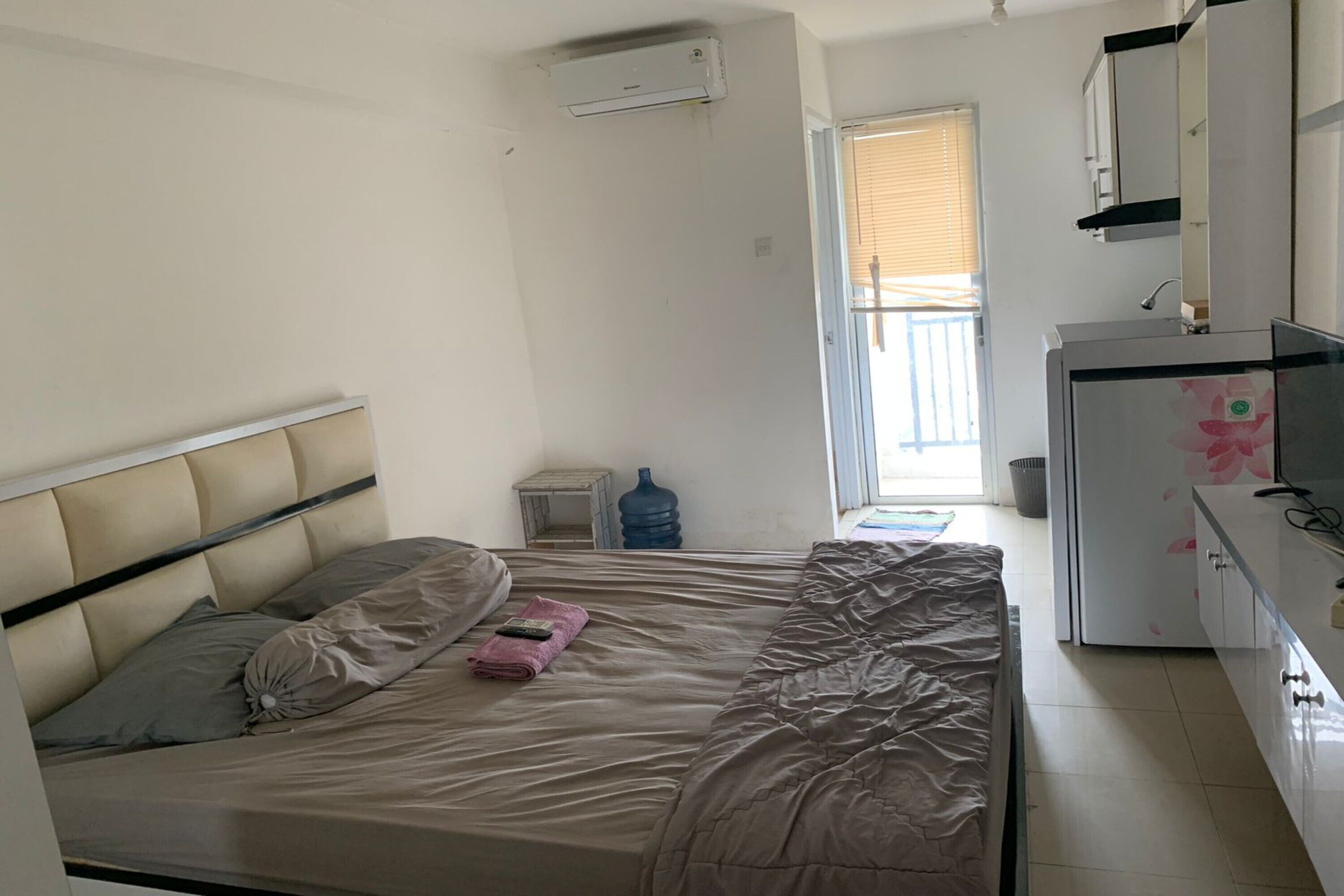 A bedroom with a bed, a small bedside table, a water dispenser, and a refrigerator.