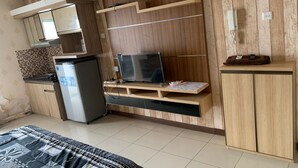 A compact living space with a kitchenette, a flat-screen TV, and a wooden cabinet. - OYO Life 93374 Andira Inn (Depok)