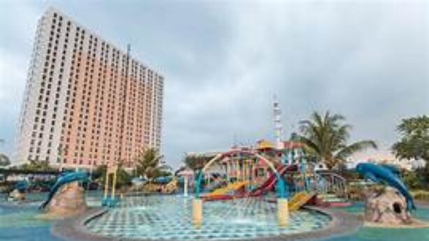A water park with slides and a circular pool, surrounded by palm trees and a tall building in the background. - OYO Life 93374 Andira Inn (Depok)