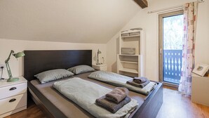 A bedroom with two beds, a nightstand with a lamp, a built-in shelf, and a view of the outdoors through a window. - House Naturalina With Pool Near Tolmin (Tolmin)