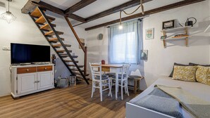 A cozy room with a wooden staircase, a television, a dining table with chairs, and a bed with patterned pillows. - House Naturalina With Pool Near Tolmin (Tolmin)