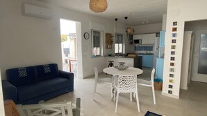 A living room with a blue sofa, white chairs, a dining table, and a kitchen area with a microwave and sink. - Addauro Villa (Alcamo Marina)